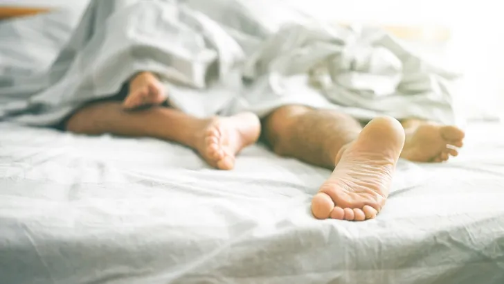 Close up of male and female feet on a bed - Loving couple having sex under under white blanket in the bedroom - Concept of sensual and intimate moment of lovers - Vintage filter - Focus on male foot