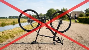 Een moderne carbon racefiets staat ondersteboven op het zadel en stuur op een geasfalteerde polderweg, met een groot rood waarschuwingskruis eroverheen geprojecteerd.