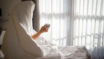 Vrouw met een kop koffie 's ochtends onder de deken thuis.