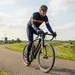 Een stevige mannelijke wielrenner op een racefiets rijdt over een dijk in de polder met een fietshelm op.