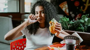 Portrait of an afro girl enjoying hamburger in a restaurant. Latin woman sucking her fingers holding a hamburger in a restaurant