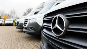 Rij witte bestelbussen op een parkeerterrein, met het Mercedes-logo groot in beeld op de voorste bestelwagen.