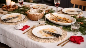 Gedekte kersttafel na afloop van het diner, met lege borden met etensresten, gebruikte bestekken en halfvolle glazen, omringd door subtiele kerstdecoratie en warme sfeerverlichting.