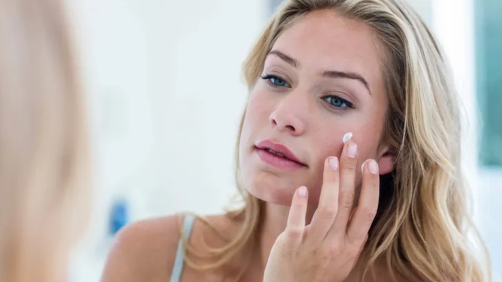 Smiling pretty woman applying cream on her face