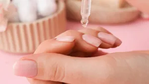 Woman applying oil onto cuticles on pink background, closeup