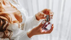 a girl in a white open dress holds purple perfume in her hands. Close-up photo