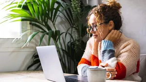 Serene young mature woman looking and reading on laptop online n