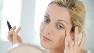 Vrouw kijkt in spiegel en brengt make-up aan naast oog