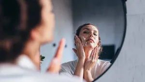 Woman washes her face in front of the mirror, applying foam to her cheeks