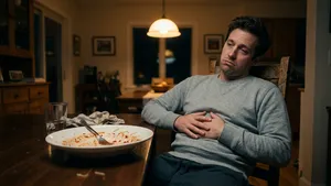 Een amateurwielrenner in vrijetijdskleding zit 's avonds met een overvolle maag en spijt aan tafel na het eten van te veel pasta voor een fietstocht.