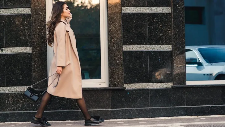 Fashionable woman with long hair walking in the city. Woman wears trendy coat and shoes.