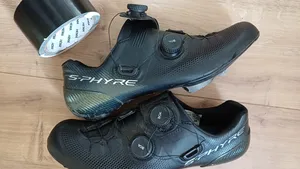Zwarte Shimano S-Phyre wielerschoenen naast een rol zwarte ducttape, klaar om met tape herfstklaar gemaakt te worden.