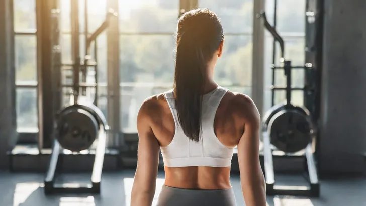 Rear close up view fit strong beautiful sporty muscular athlete woman trainer bodybuilder back wear sportswear training in sunny gym indoors, bodybuilding workout exercises background concept