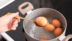 Vrouw met lepel en gekookt ei boven kookpan in de keuken, close-up.