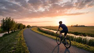 Een eenzame wielrenner met helm fietst over een lege dijk in een Nederlands landschap tijdens zonsondergang.