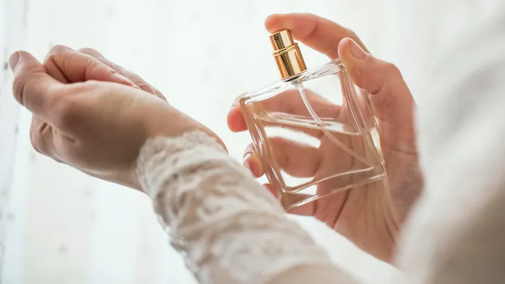Vrouw sprayt parfum op haar pols, waarbij ze erop let dat ze de polsen niet over elkaar wrijft om de geur te behouden.