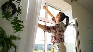 Een vrouw wast handmatig de ramen van het huis met een doek en een schoonmaakspray tijdens de voorjaarsschoonmaak-light.