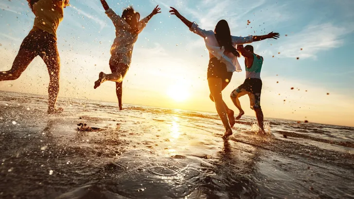 Happy friends at beach party runs to sunset water