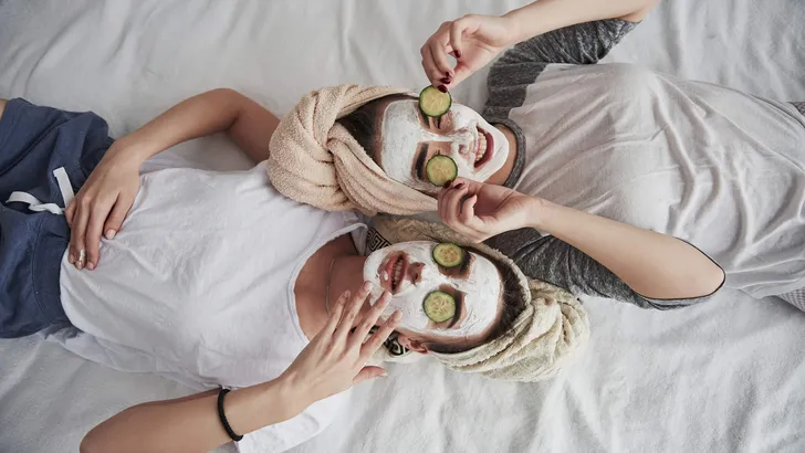 Taking off these things. Lying on the white bed. Top view. Conception of skin care by using white mask and cucumbers on the face