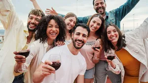 Group of young adult best friends having fun toasting a red wine glasses at rooftop reunion or birthday party, drinking alcohol. Happy people enjoying on a social gathering celebrating together
