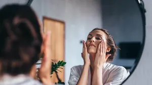 Woman applies foam to her face, cleansing her skin.