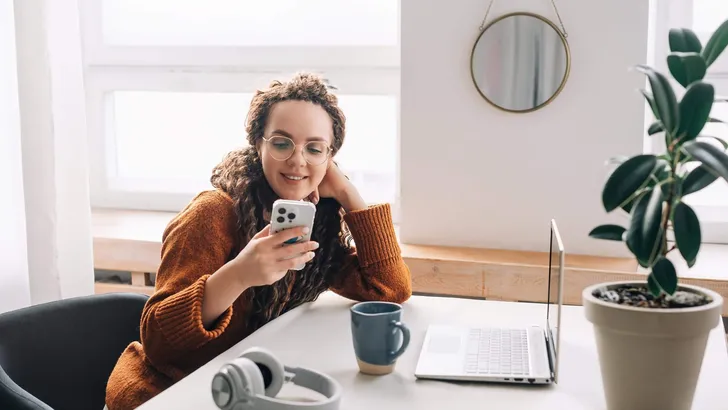 Smiling young woman texting on cellphone while working remotely at home office technology and modern lifestyle concept. Happy young woman using smartphone for remote work and learning at home office