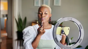 Young African influencer putting on lip gloss during a vlogcast