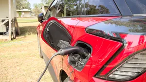 Elektrische auto (EV) met aangesloten Vehicle-to-Load (V2L) type 2 adapter op een camping bij een vakantiehuisje.