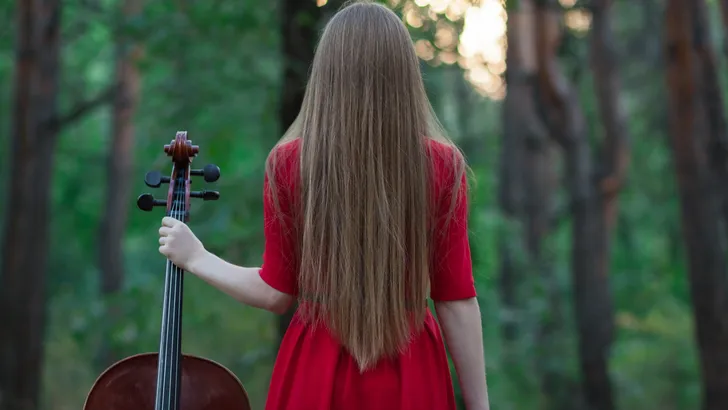 Woman in red dress with cello in the forest