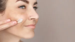 Caucasian woman's face with freckles or age spots, she smears cream on her cheek with her fingers, nice cream swatch, copy space for text