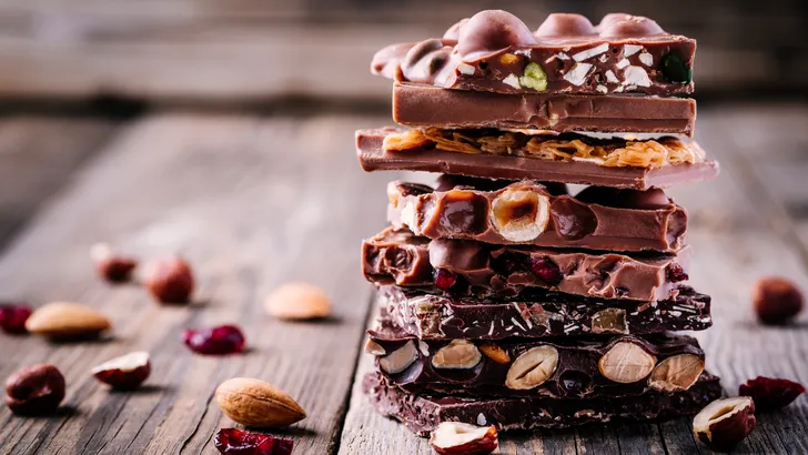 Stack of milk and dark chocolate with nuts, caramel and fruits and berries on wooden rustic background.