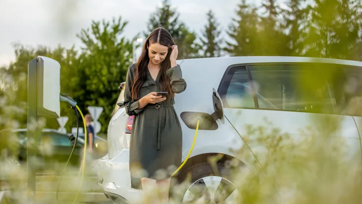 Woman using mobile phone while waiting for electric car to charge in the parking lot