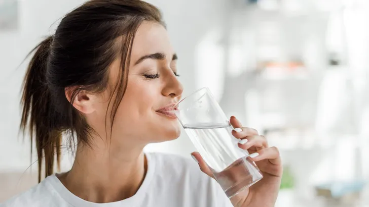 smiling girl holding drinking water from glass in the morning