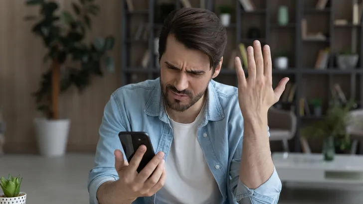 Gefrustreerde man kijkt naar zijn telefoonscherm.