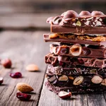 Stack of milk and dark chocolate with nuts, caramel and fruits and berries on wooden rustic background.