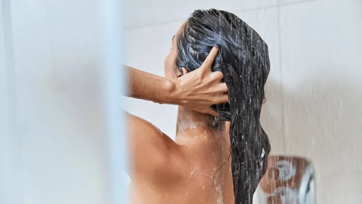 Brunette young woman washing her hair in shower