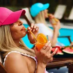 Two young attractive women are sitting in chairs by the pool and enjoying themselves