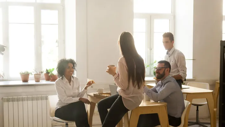 Smiling multiracial colleagues talking while eating pizza at off