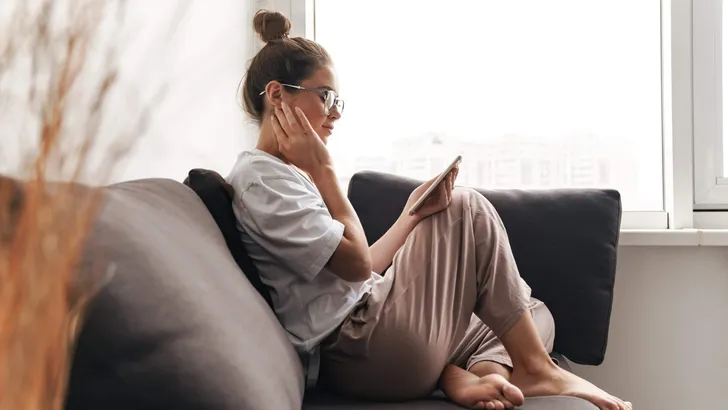 Image of concentrated woman using cellphone while sitting on sof