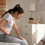 Young woman suffering from stomach ache on bed at home, space fo