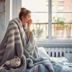 A woman in a blanket in a cold apartment.