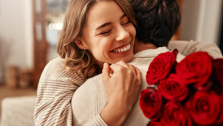 Vrouw omhelst man nadat ze een bos rode roze krijgt.