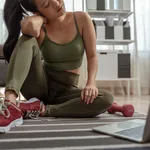 A sporty woman in sportswear is sitting on the floor with dumbbells and is using a laptop at home in the living room.Exercise indoors during quarantine. Exercise, Workout at home activities.