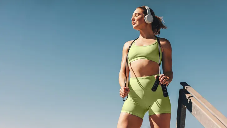 Female athlete in her 30s outdoors taking a break from her cardio workout, holding a skipping rope and wearing sportswear