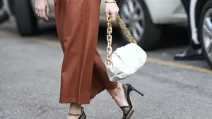 Hoe zwaar mag een handtas zijn? – Streetstyle-foto van vrouw in bruinleren rok met zwarte hakken en witte handtas.