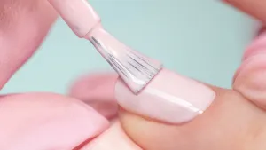 Close-up foto van nagel die wordt gelakt met lichtroze nagellak tegen lichtblauwe achtergrond.