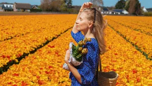 Nederland in top 10 beste landen voor je huid. – Foto van vrouw in de zon in tulpenveld in blauwe jurk.