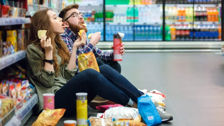 Couple sitting on the supermarket floor and eating snacks