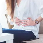 A woman having stomachache sitting on sofa and holding her belly by hands.