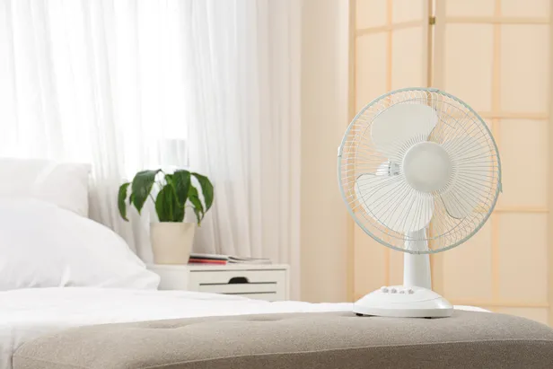 Witte ventilator naast bed in de slaapkamer.